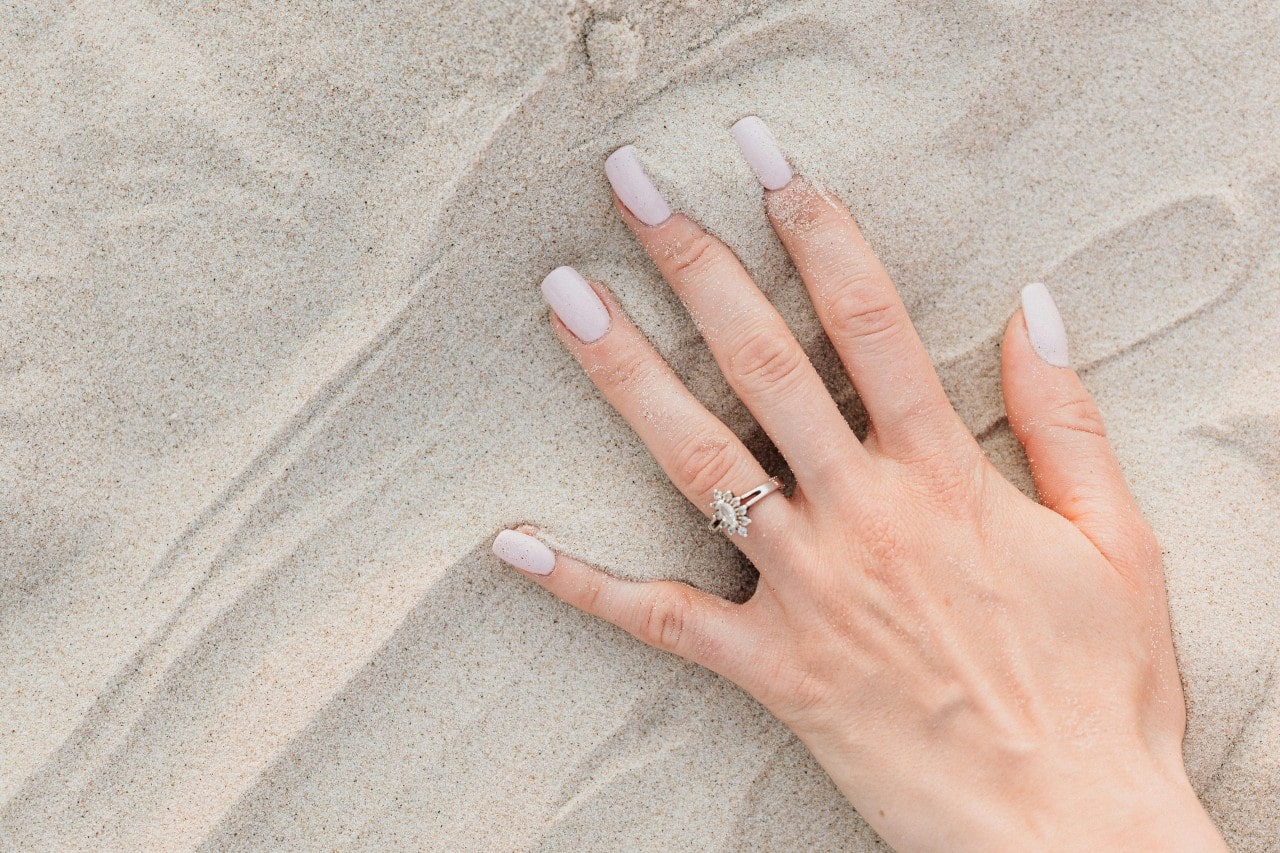 a woman’s hand in the san, adorned with a marquise cut halo engagement ring