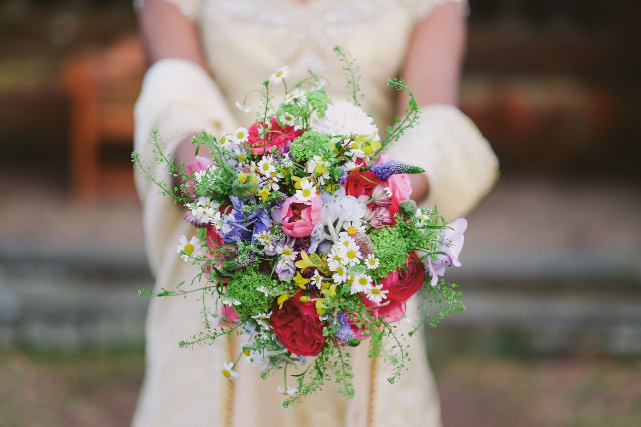 A bride holding out her colorful bouquet of multiple types of flowers