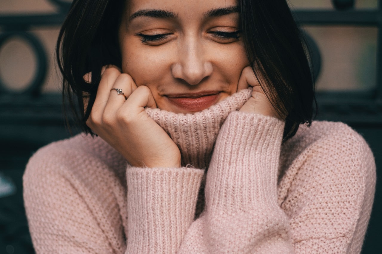 A smiling woman bundled up in a pink turtleneck sweater sits inside.
