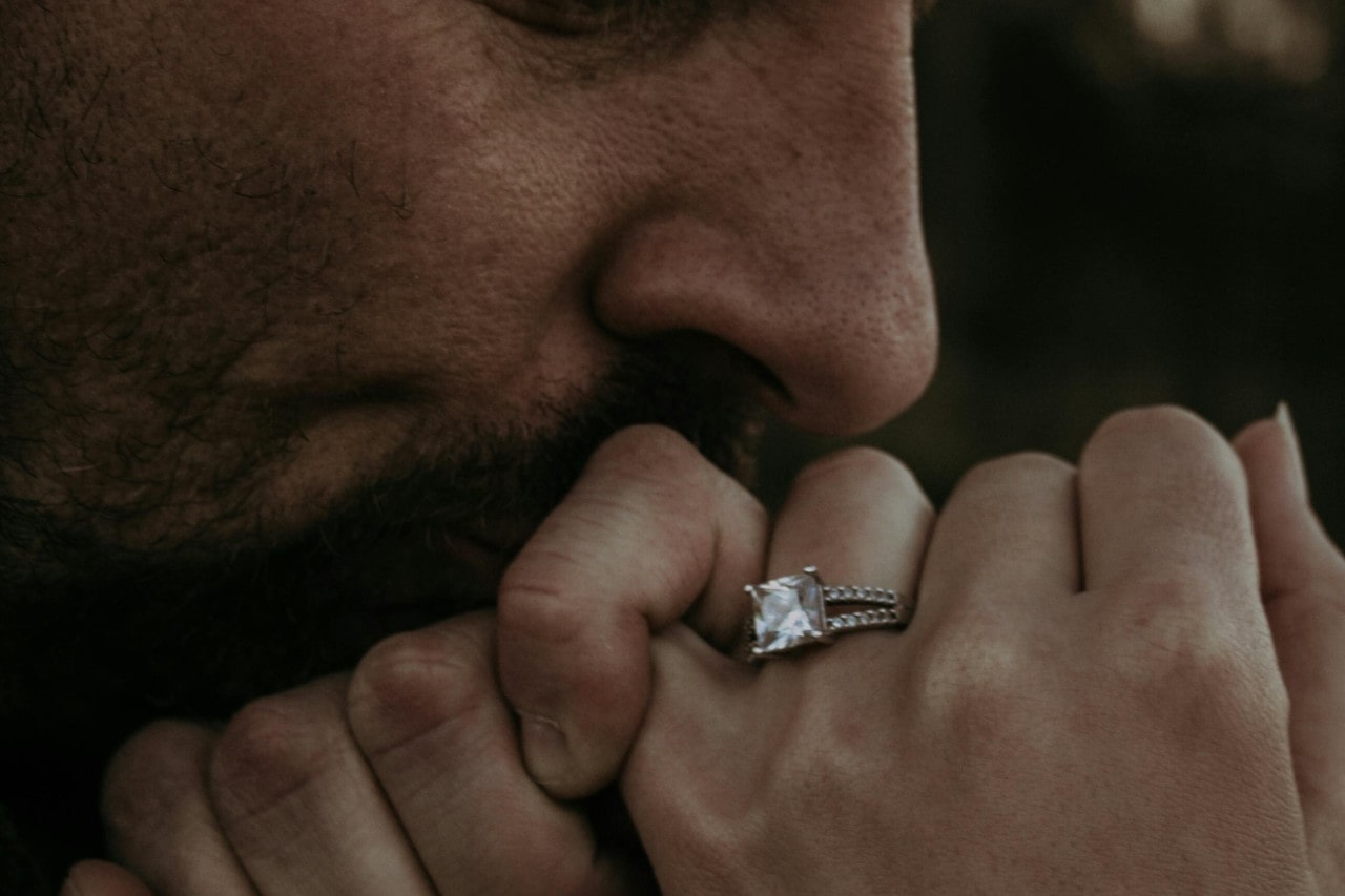 a man kissing a woman’s hand who is wearing a large diamond engagement ring