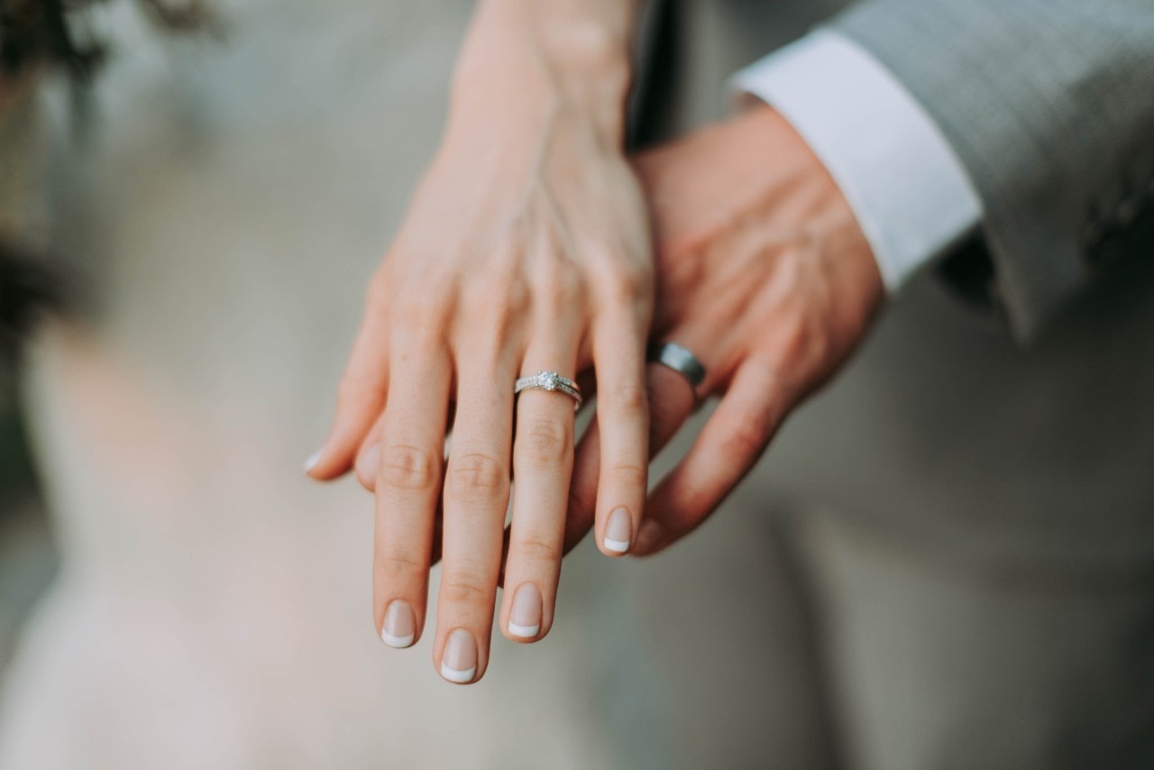 a bride and groom’s outstretched hands, both wearing white gold wedding bands