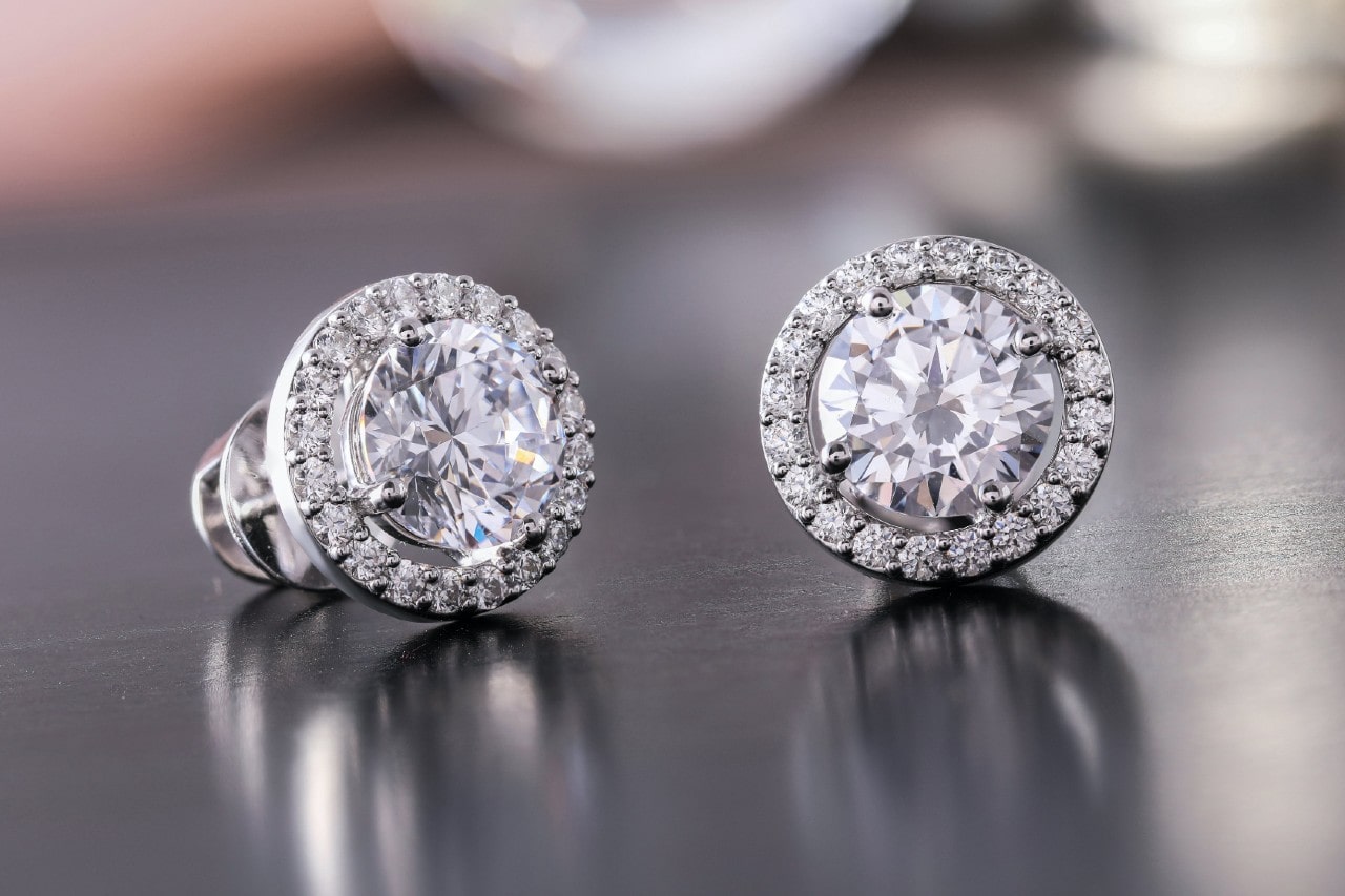 a pair of white gold diamond stud earrings with diamond halos on a metallic surface