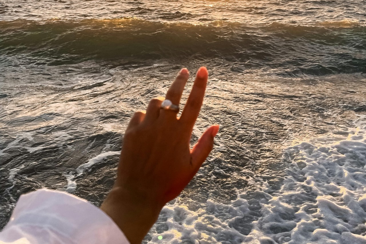 a woman’s hand extended towards the ocean, adorned with a large pearl ring