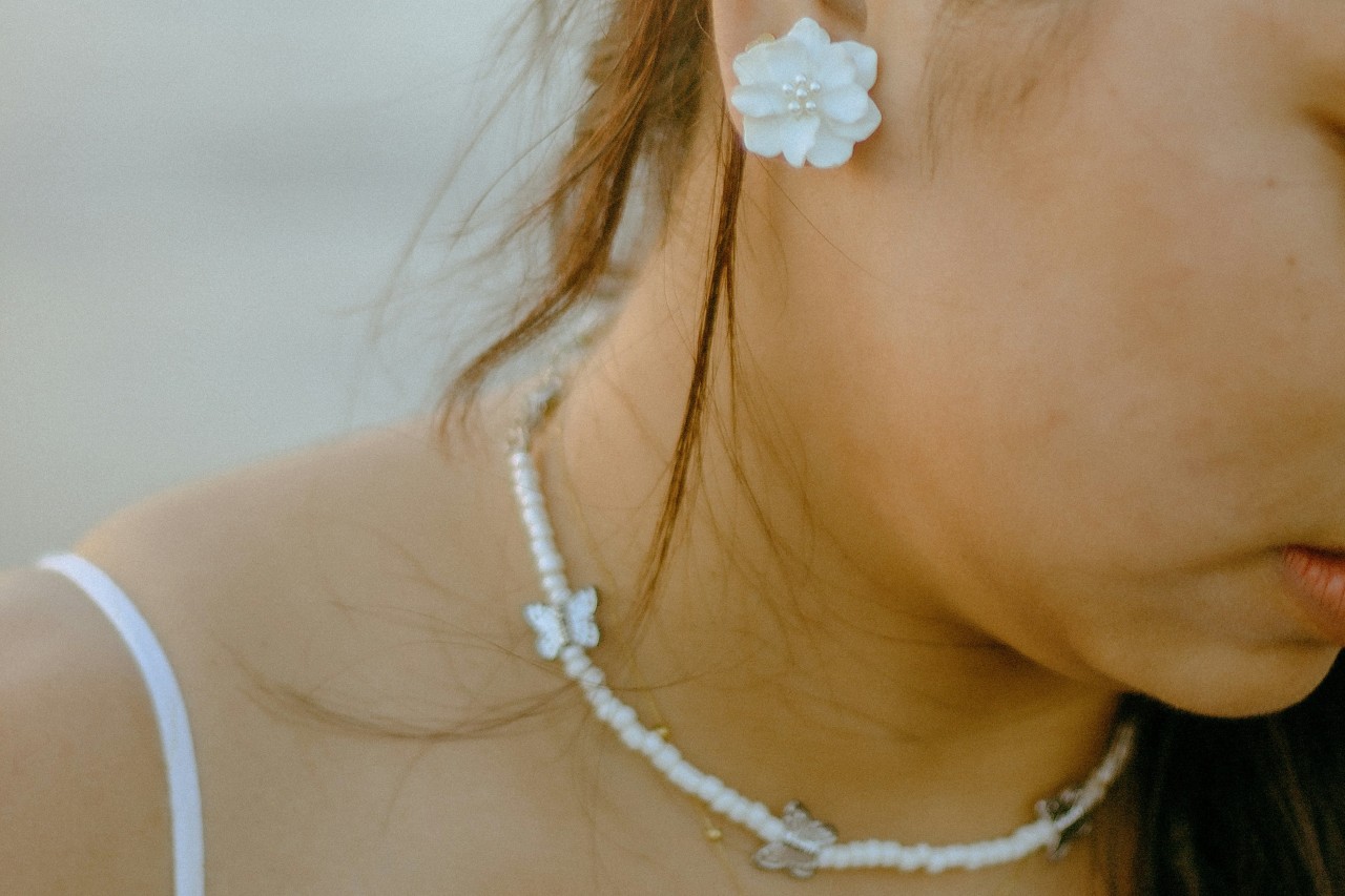 a woman looking away from the camera wearing a butterfly necklace and flower earring