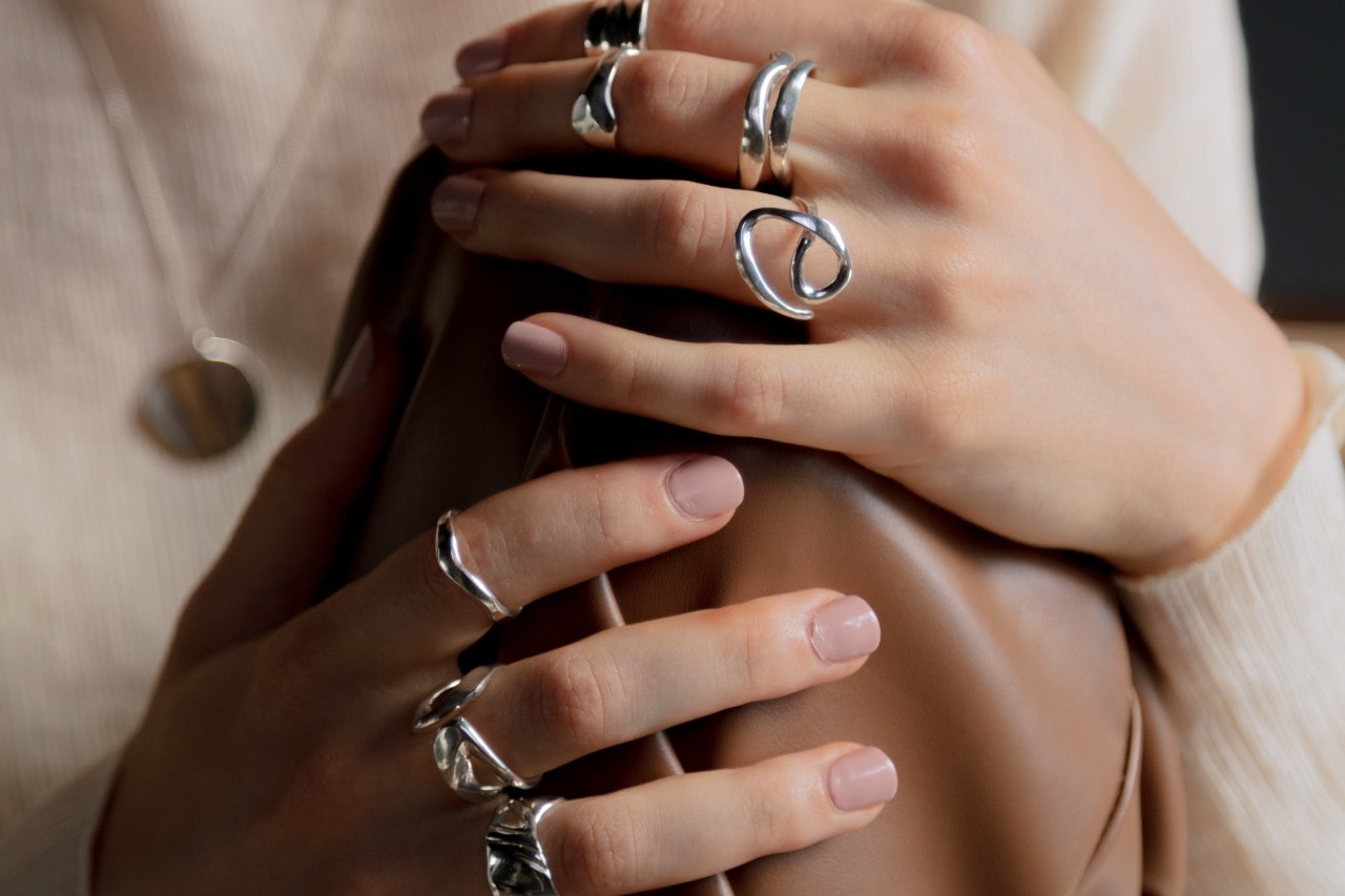 a woman’s hands resting on her knee, wearing sparkly silver fashion rings