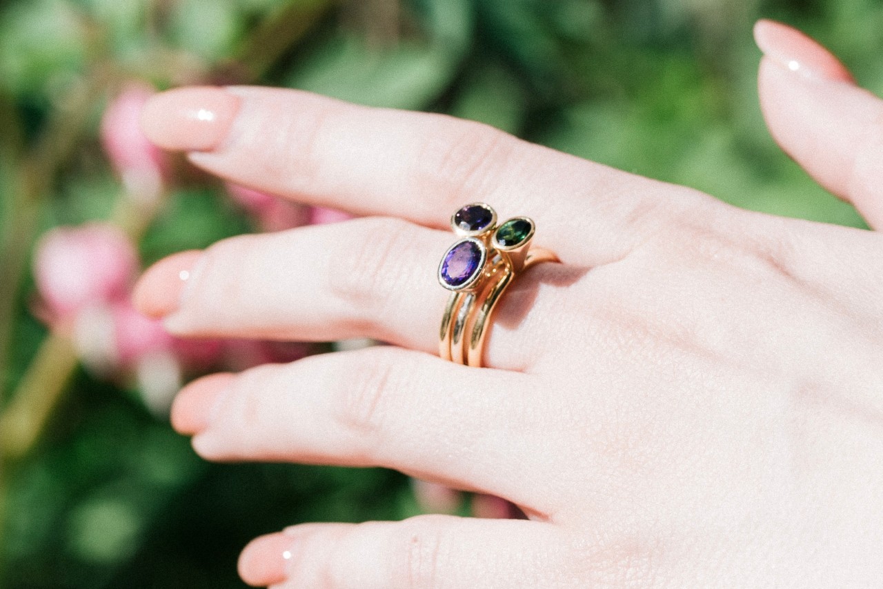 a woman’s outstretched hand wearing a stack of three matching gemstone rings