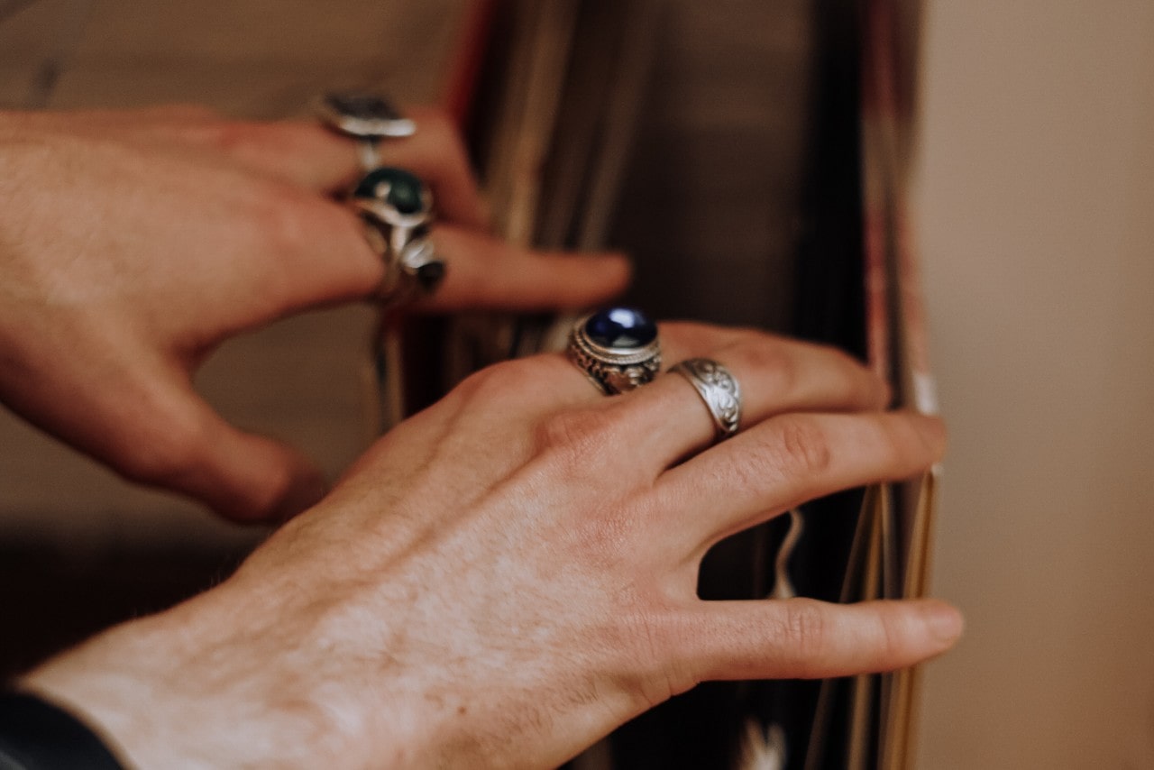 a person’s hands looking through records and wearing a stack of fashion rings