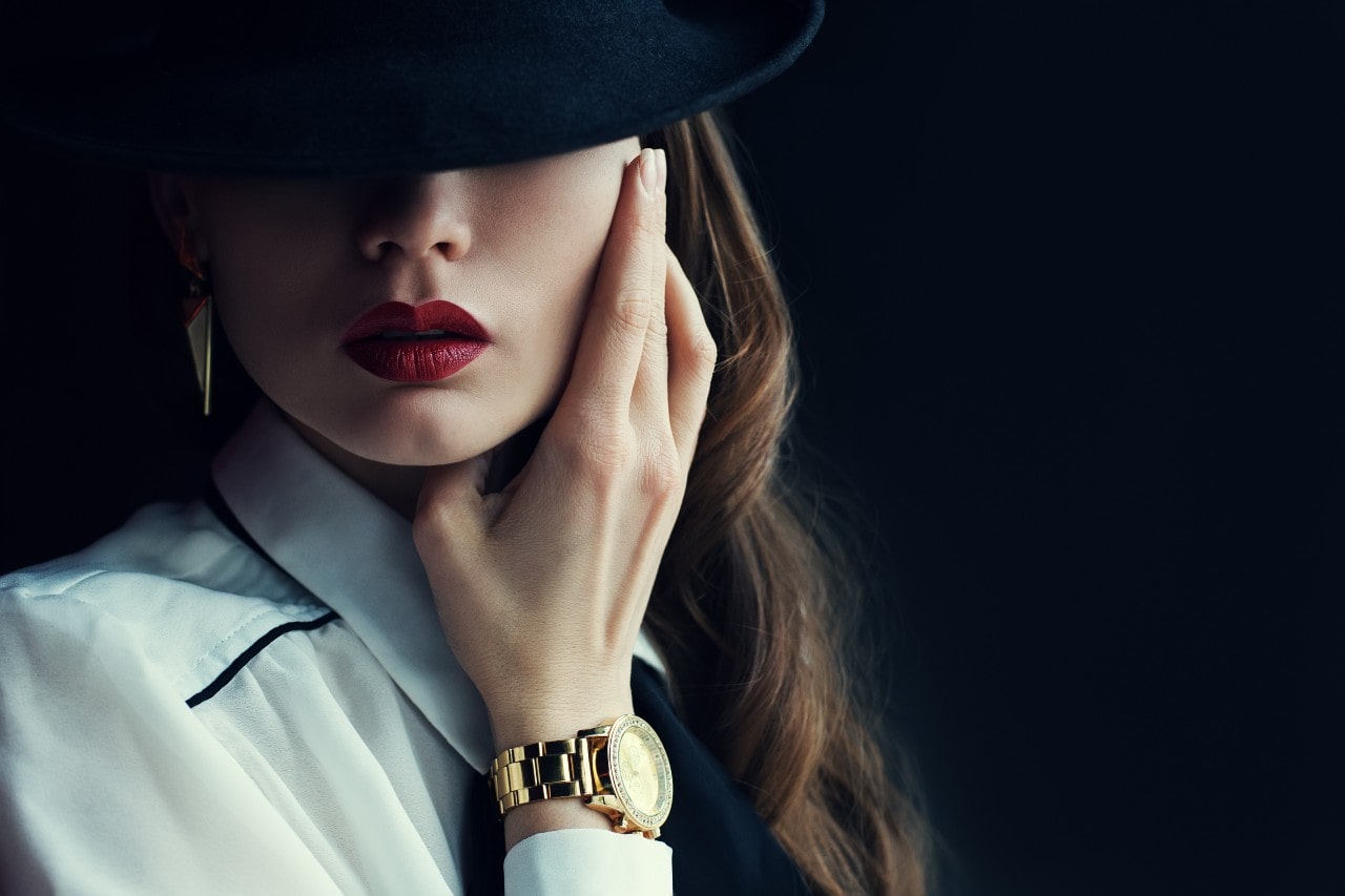 a woman with her hand lifted to her face, wearing a yellow gold dress watch