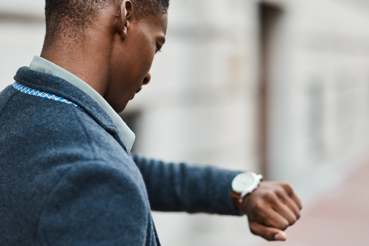 a man in a grey coat looking down at his dress watch