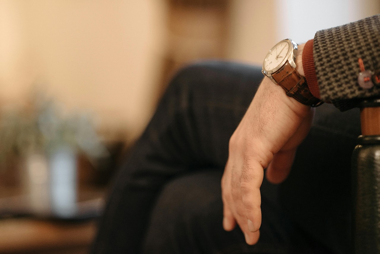 close up image of a man’s wrist resting on a chair arm–adorned with a dress watch