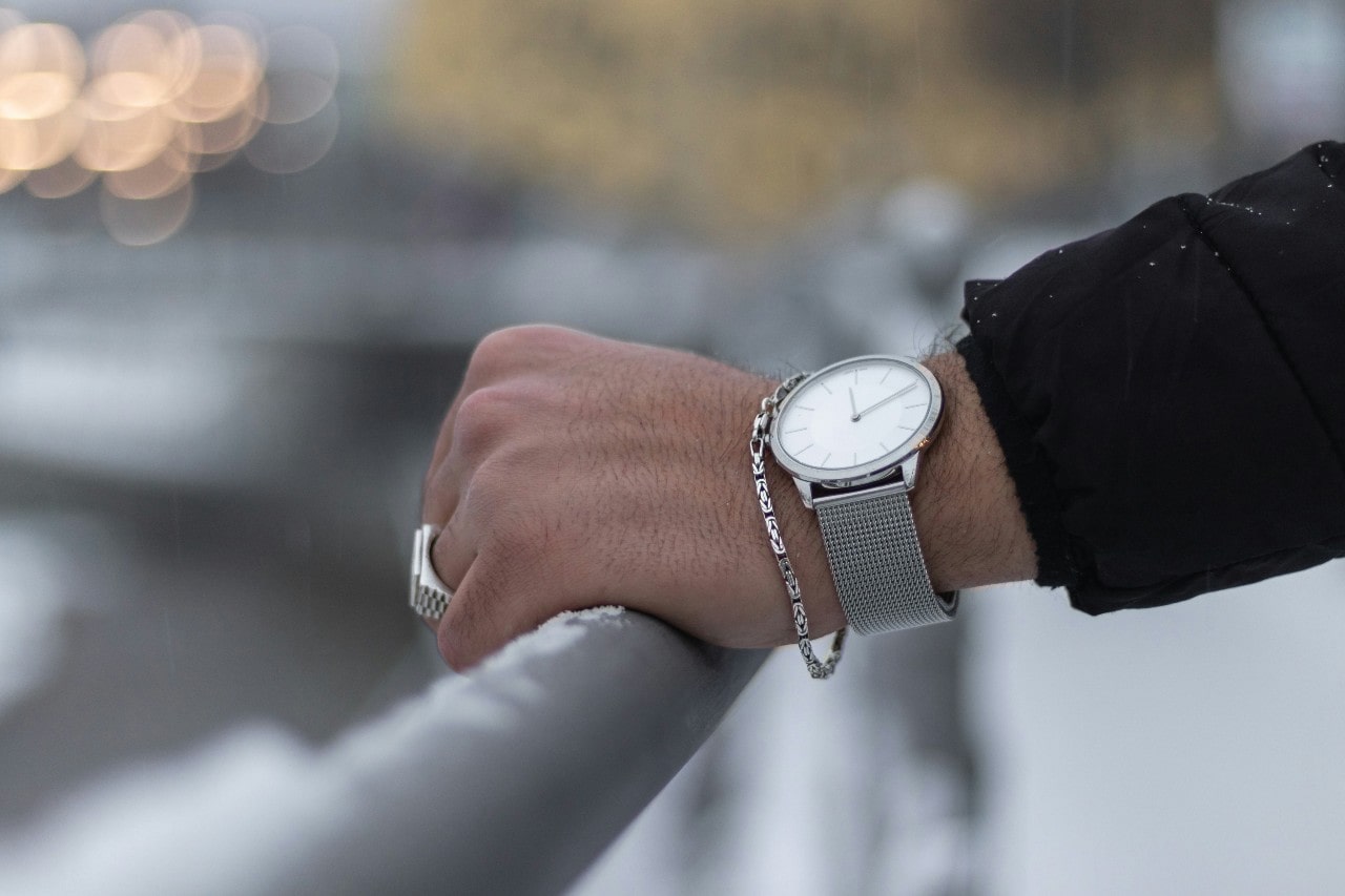 a man’s hand resting on a rail, adorned with a silver dress watch