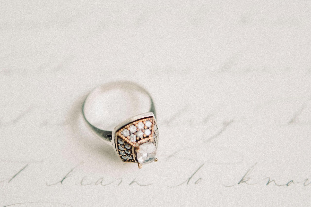 a mixed metal diamond engagement ring resting on paper with cursive writing on it