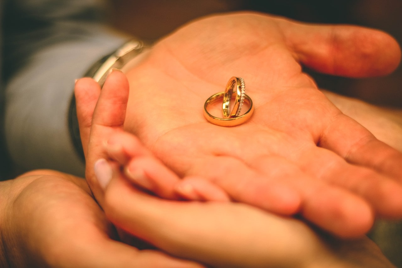 a couples’ hands stacked together, holding a pair of matching wedding bands.