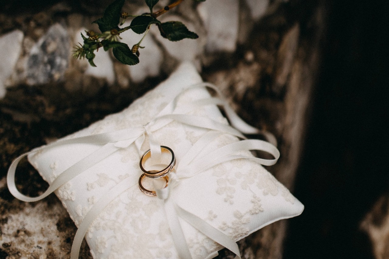 a matching set of wedding bands tied with ribbon on a white pillow