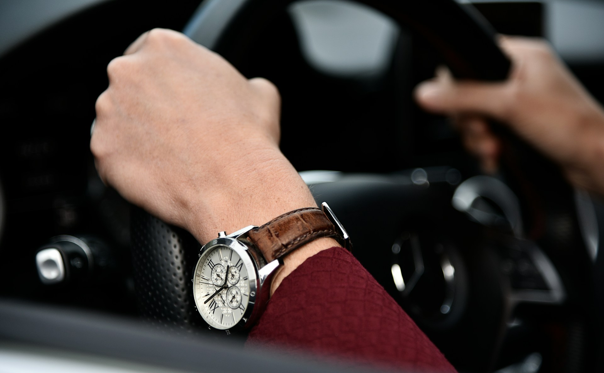 a person’s hands gripping a steering wheel and wearing a high end watch