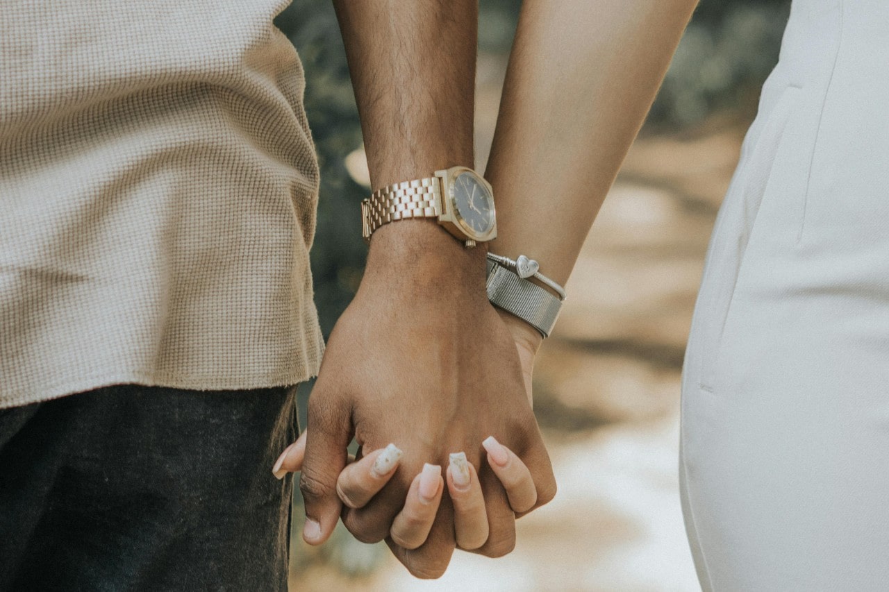 a couple holding hands, the man wearing a yellow gold luxury watch