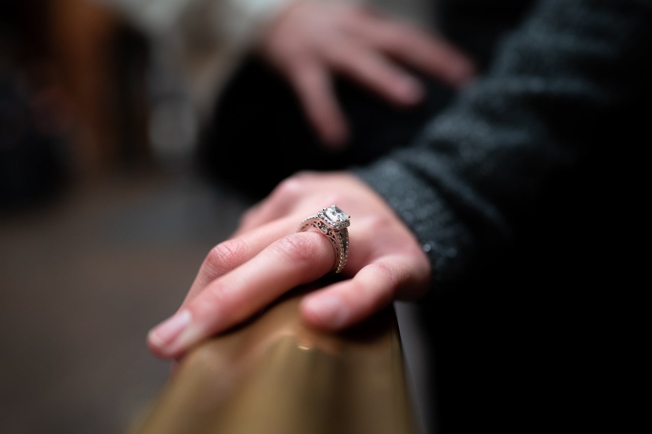 a woman’s hand resting on a bar, wearing a vintage-inspired engagement ring