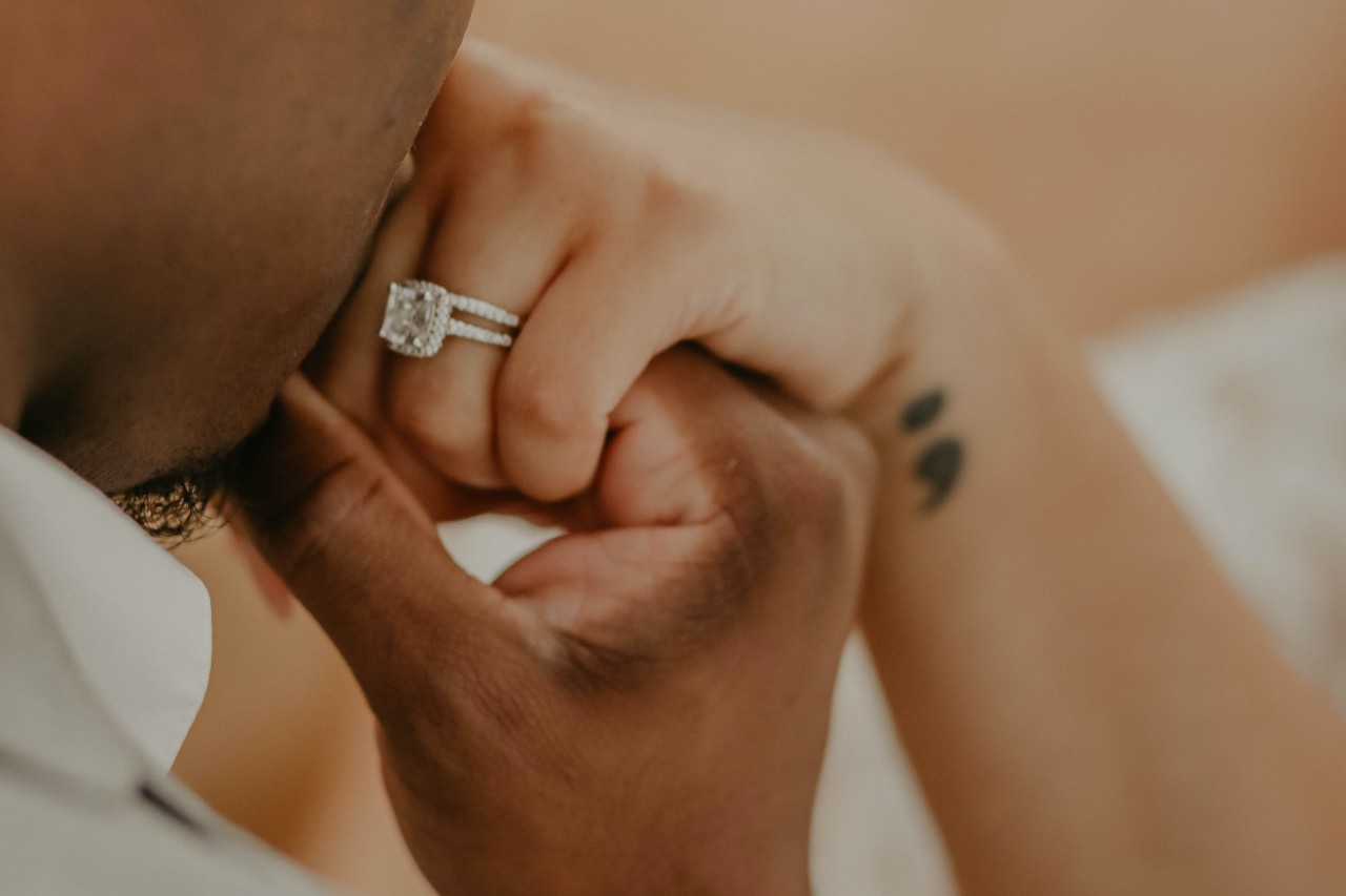 A man kissing the hand of his bride with a clear view of her halo diamond ring