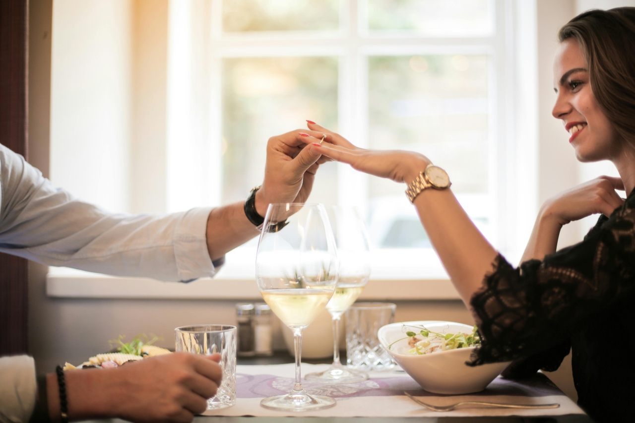 A couple at lunch, and a man is slipping an engagement ring on the woman’s finger