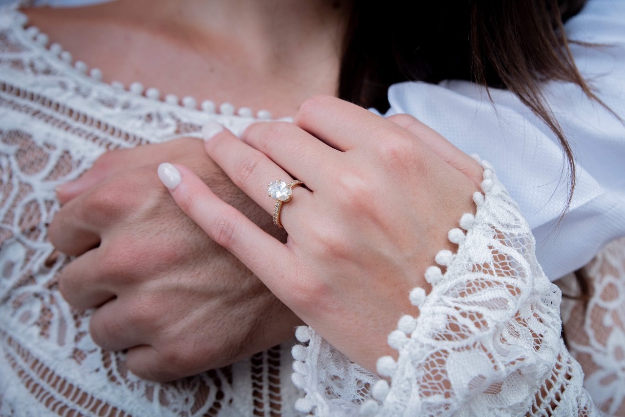 A man resting his arm on his bride and her resting her hand on his arm, with a view of her side stone ring